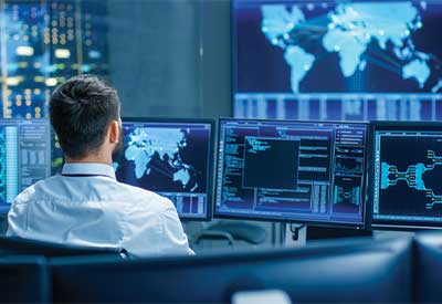 Person monitoring global cybersecurity data on multiple screens.